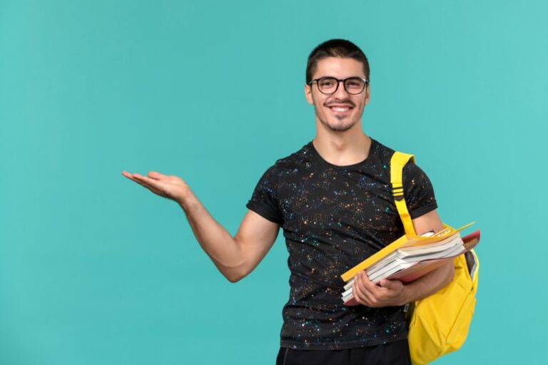 front-view-of-male-student-in-dark-t-shirt-yellow-backpack-holding-files-and-books-smiling-on-light-blue-wall-1024x683